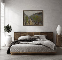 Busy Parisian boulevard cityscape print in a dark wood frame above a rattan bed on a plaster wall