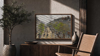 Busy Parisian boulevard cityscape print in a wood frame above a fluted sideboard beside an olive tree