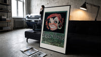 Grinning woman's face with earring print in a slim black frame leaning on a dark sofa in a concrete print studio
