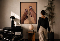 Cowhide Mules and Chain Anklet print in a black frame on a sunlit wall with a viewer