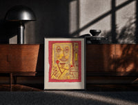 Black-framed Abstract face with small figures print on a moody console with designer coffee-table books