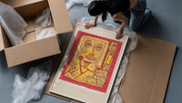 Abstract face with small figures framed print being unpacked from protective bubble wrap and a box