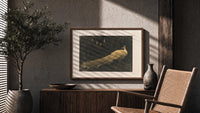 White peacock in landscape print in a wood frame above a fluted sideboard beside an olive tree