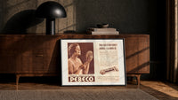 Woman holding hand mirror print in a black frame leaning against a walnut console in lamplight