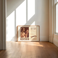 Woman holding hand mirror print in an oak frame on a sunlit wood floor beneath tall window light