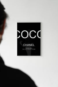 Person looking at a black Coco Chanel quote poster displayed on a white gallery wall