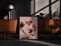 Black-framed Pink Drink, Cherries and Perfume print on the floor in front of a dark wooden console