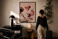 Pink Drink, Cherries and Perfume print in a black frame on a sunlit plaster wall, a woman looking on beside a mushroom lamp