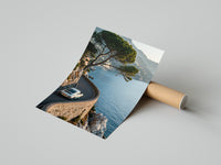Hands unrolling a Porsche 911 Amalfi coast art print on polished concrete revealing bright Mediterranean waters