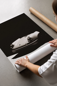 Person unrolling a black and white Porsche 911 poster showing the sleek sports car front view