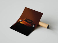 Front-facing Porsche 911 with glowing headlights in amber studio lighting shown as a rolled poster print