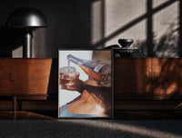 Black-framed Pouring a Sparkling Drink print on the floor in front of a dark wooden console