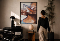 Pouring a Sparkling Drink print in a black frame on a sunlit plaster wall, a woman looking on beside a mushroom lamp