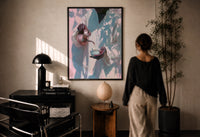 Pouring Tea in a White Robe print in a black frame on a sunlit plaster wall, a woman looking on beside a mushroom lamp