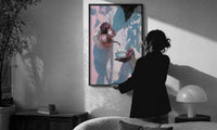 Pouring Tea in a White Robe print in a slim black frame being hung on a sunlit wall in a monochrome room