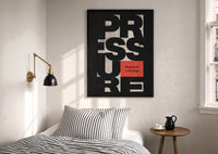 Pressure Is a Privilege print in a black frame above a bed with striped linens, a brass wall lamp and a sunlit window