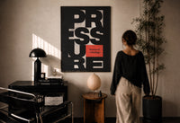 Pressure Is a Privilege print in a black frame on a sunlit plaster wall, a woman looking on beside a mushroom lamp
