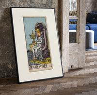 Queen seated on throne holding cup print in a black frame leaning beside a vintage door on parquet