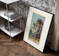 Queen seated on throne holding cup poster in a black frame leaning beside a shelf in a raw-plaster loft