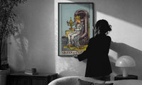 Queen of Cups print in a slim black frame being hung on a sunlit wall in a monochrome room