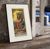 Crowned queen holding pentacle on throne print in a black frame leaning beside a vintage door on parquet