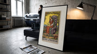 Crowned queen holding pentacle on throne print in a slim black frame leaning on a dark sofa in a concrete print studio