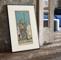 Queen of Swords tarot card print in a black frame leaning beside a vintage door on parquet