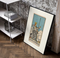 Queen of Swords tarot card poster in a black frame leaning beside a shelf in a raw-plaster loft