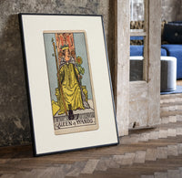 Queen of Wands tarot card print in a black frame leaning beside a vintage door on parquet