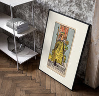 Queen of Wands tarot card poster in a black frame leaning beside a shelf in a raw-plaster loft