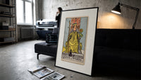Queen of Wands tarot card print in a slim black frame leaning on a dark sofa in a concrete print studio