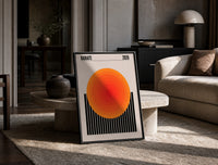 Radiate 2026 Orange Sun print on the floor, leaning against a travertine table