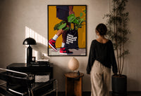 Plant Tote and Red High-Tops print in a black frame on a sunlit plaster wall, a woman looking on beside a mushroom lamp
