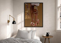 Red Platform Heels and Mesh Bag print in a black frame above a bed with striped linens, a brass wall lamp and a sunlit window