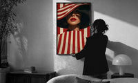 Red Stripes and a Wide Hat print in a slim black frame being hung on a sunlit wall in a monochrome room