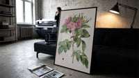 Pink wild roses botanical study print in a slim black frame leaning on a dark sofa in a concrete print studio