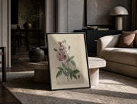 Pink rose botanical illustration print in a black frame leaning on a travertine table in a sunlit lounge