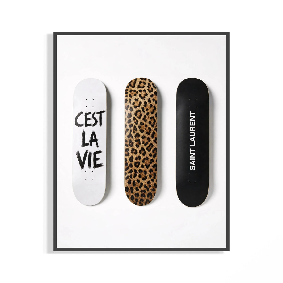 Trio of leopard print and white script Saint Laurent skate decks shown in a black display frame on a wall
