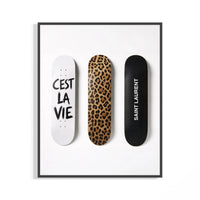 Trio of leopard print and white script Saint Laurent skate decks shown in a black display frame on a wall