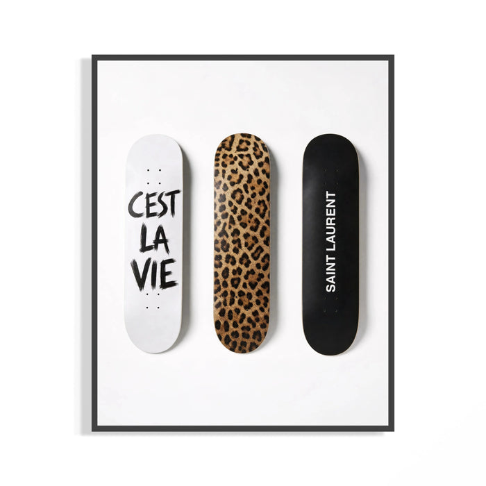 Trio of leopard print and white script Saint Laurent skate decks shown in a black display frame on a wall