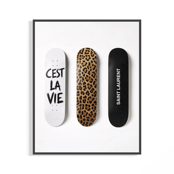 Trio of leopard print and white script Saint Laurent skate decks shown in a black display frame on a wall