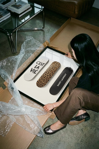 Hands unrolling a leopard print and black Saint Laurent skateboard design printed on white paper