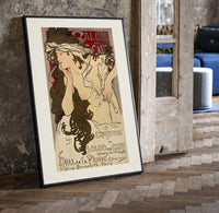 Woman with flowing hair holding feather print in a black frame leaning beside a vintage door on parquet