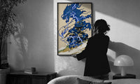 Samurai swordsman with blue lightning dragon print in a slim black frame being hung on a sunlit wall in a monochrome room