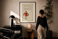 Santa Christmas Greeting print in a black frame on a sunlit plaster wall, a person looking on beside a mushroom lamp
