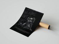 Seated black KAWS companion on dark graffiti-text background, unrolled print laid beside a cardboard tube on gray