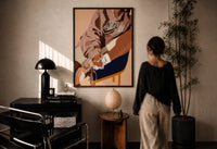Black Woman in a Brown Crewneck print in a black frame on a sunlit plaster wall, a woman looking on beside a mushroom lamp