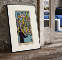 Seven Cups of Wands tarot card print in a black frame leaning beside a vintage door on parquet