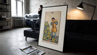 Man leaning on staff with pentacles print in a slim black frame leaning on a dark sofa in a concrete print studio