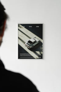 Silver Porsche 911 captured in moody shadow and light composition, poster displayed beside a mailing tube
